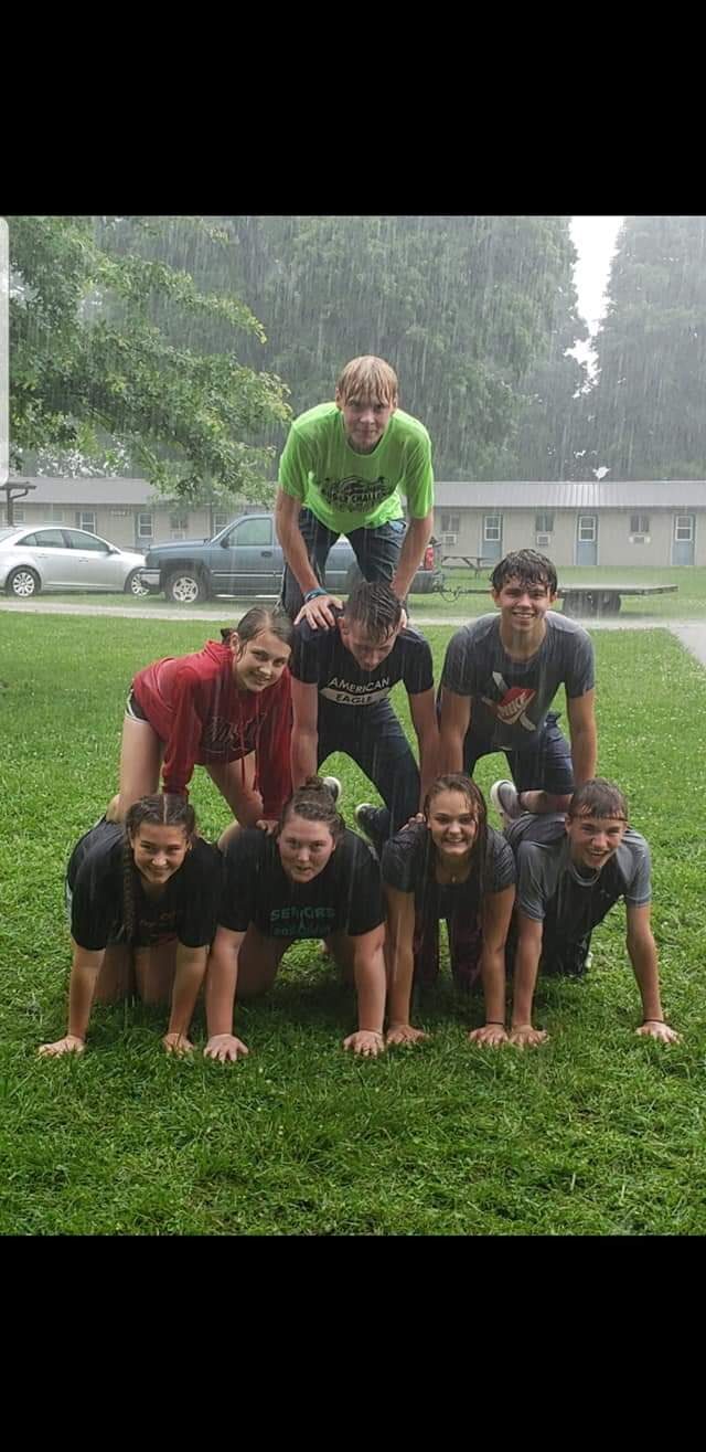 Campers forming a human pyramid on the lawn during a rainstorm