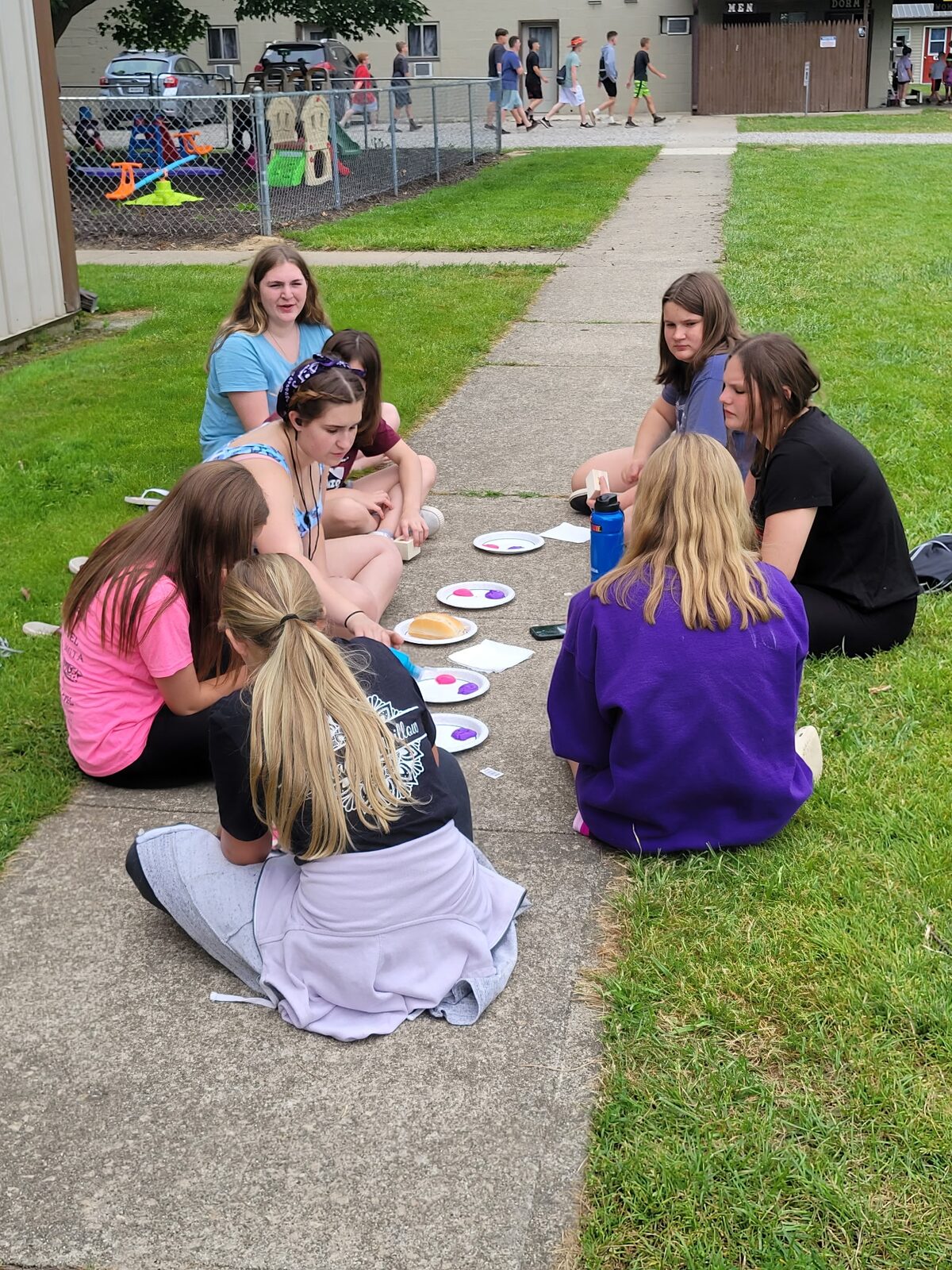 Campers sitting on a sidewalk working on a craft project together